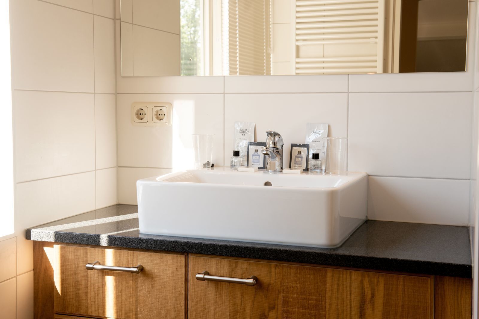 Un bagno con lavandino bianco, mobiletti in legno e specchio sopra il lavandino.
