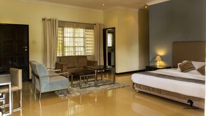 A hotel room with a bed, a sofa, a coffee table, a desk, and a window with curtains. - Cedar Place (Blantyre)