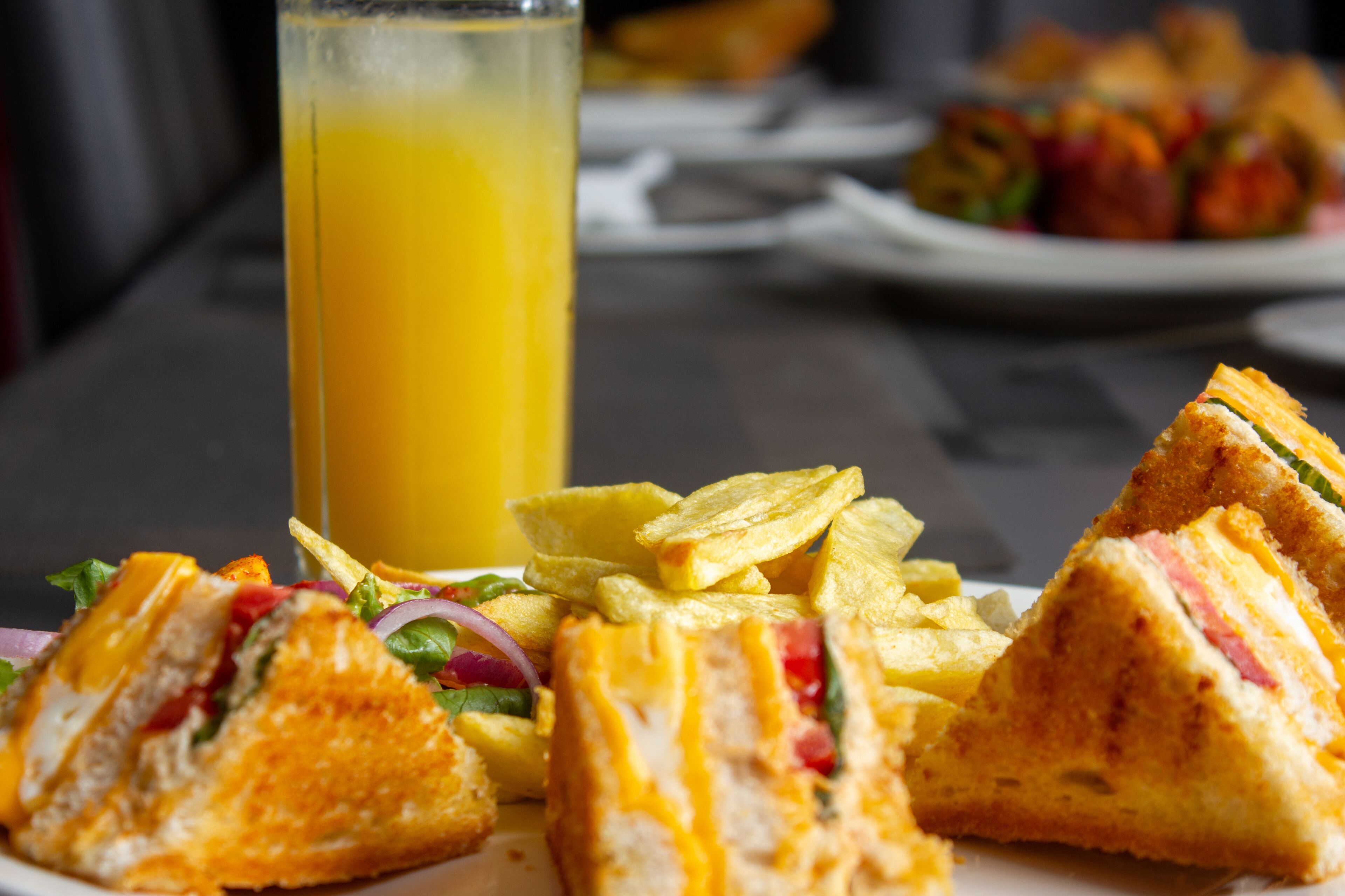 Un plato de sándwiches y papas fritas, con un vaso de jugo de naranja al fondo.