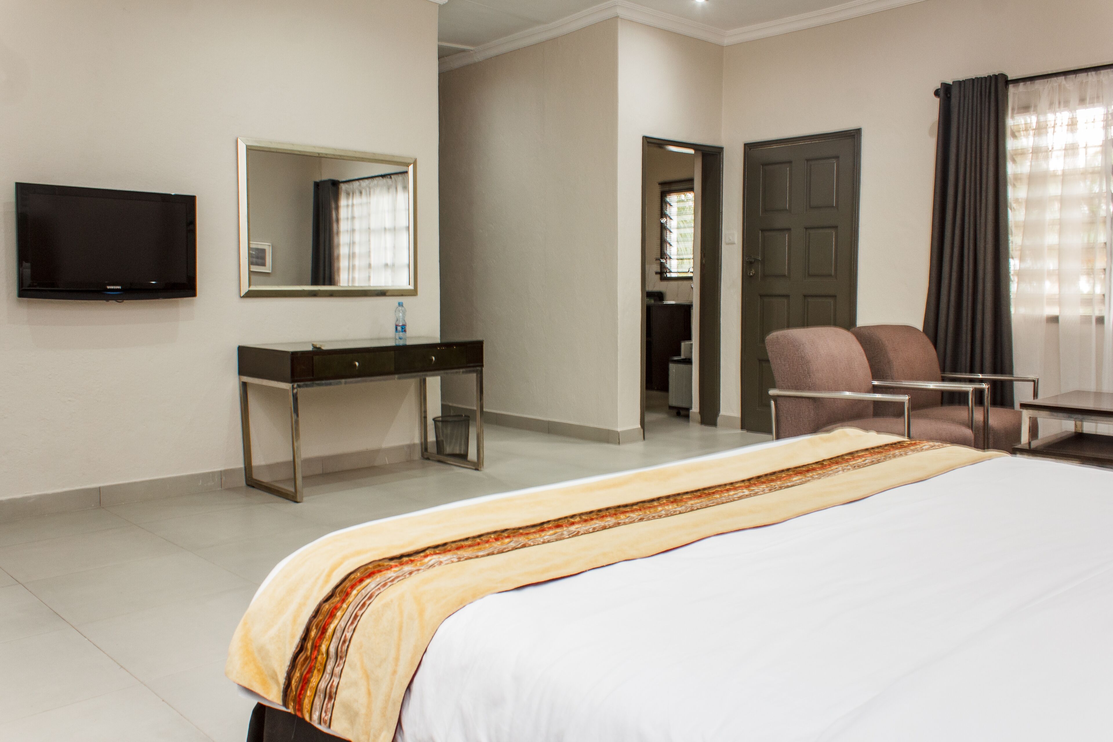 A hotel room with a bed, a desk, a chair, a television, and a door leading to a bathroom.