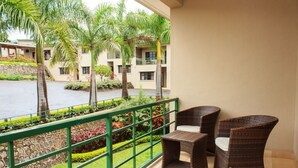 A balcony with wicker furniture, a stone wall, and a view of a building with balconies and palm trees. - Cedar Place (Blantyre)