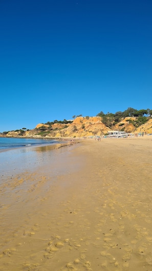 A beach with clear blue water, sandy shore, and a building with a white facade.