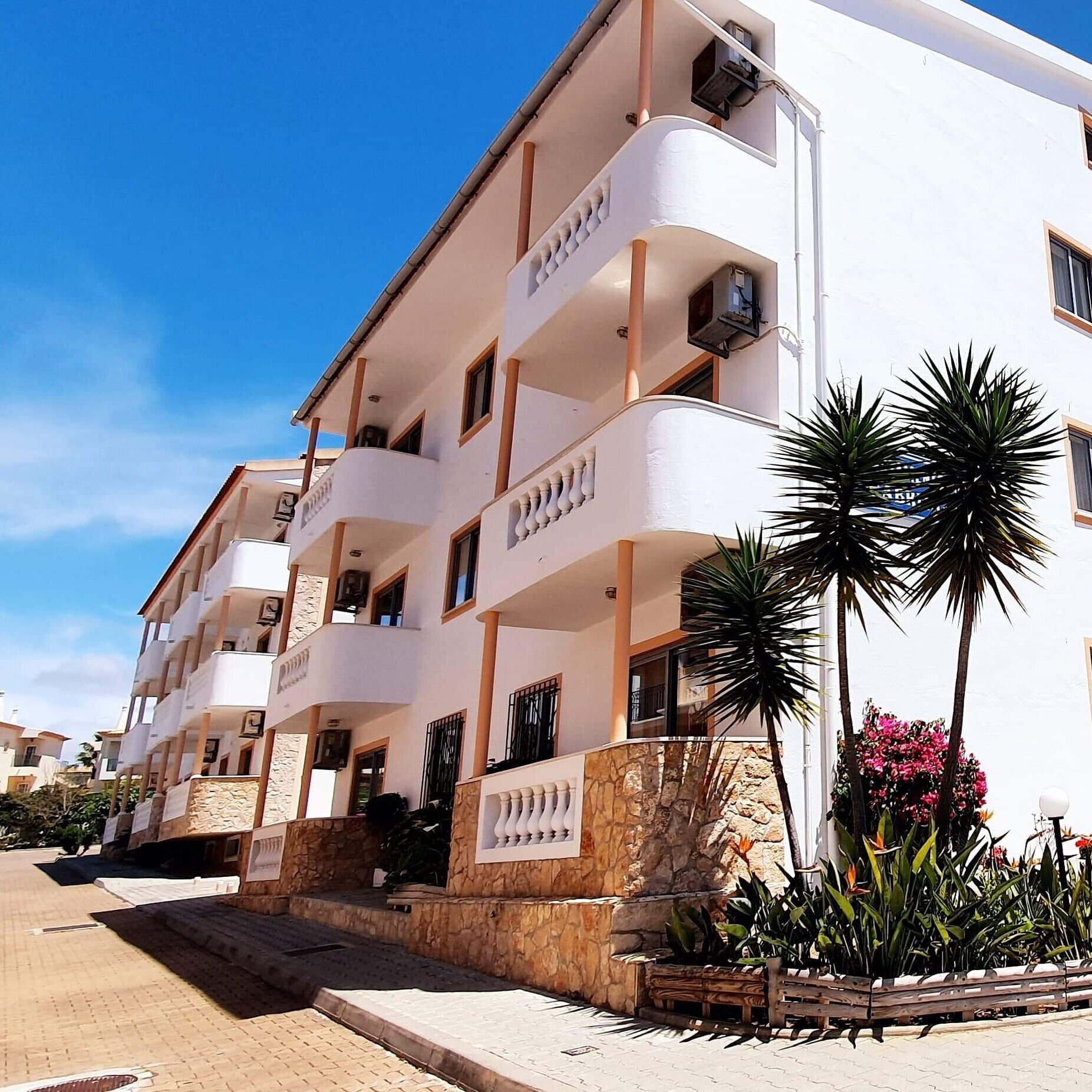 A multi-story building with balconies, a stone base, and potted plants.
