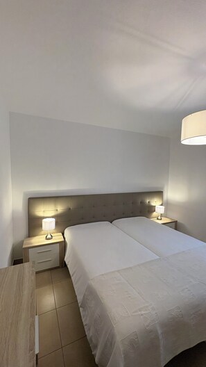 A hotel room with a large bed, two bedside tables with lamps, a wooden nightstand, and a ceiling light.