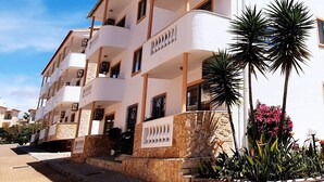 Un immeuble à plusieurs étages, doté de balcons, d’une base en pierre et de plantes en pot.