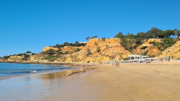 Une plage avec une eau d’un bleu limpide, un rivage sablonneux et un bâtiment à la façade blanche.
