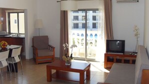 Une chambre d’hôtel équipée d’un canapé, d’un fauteuil, d’une télévision, d’une table à manger, de chaises et d’un balcon avec des rideaux.