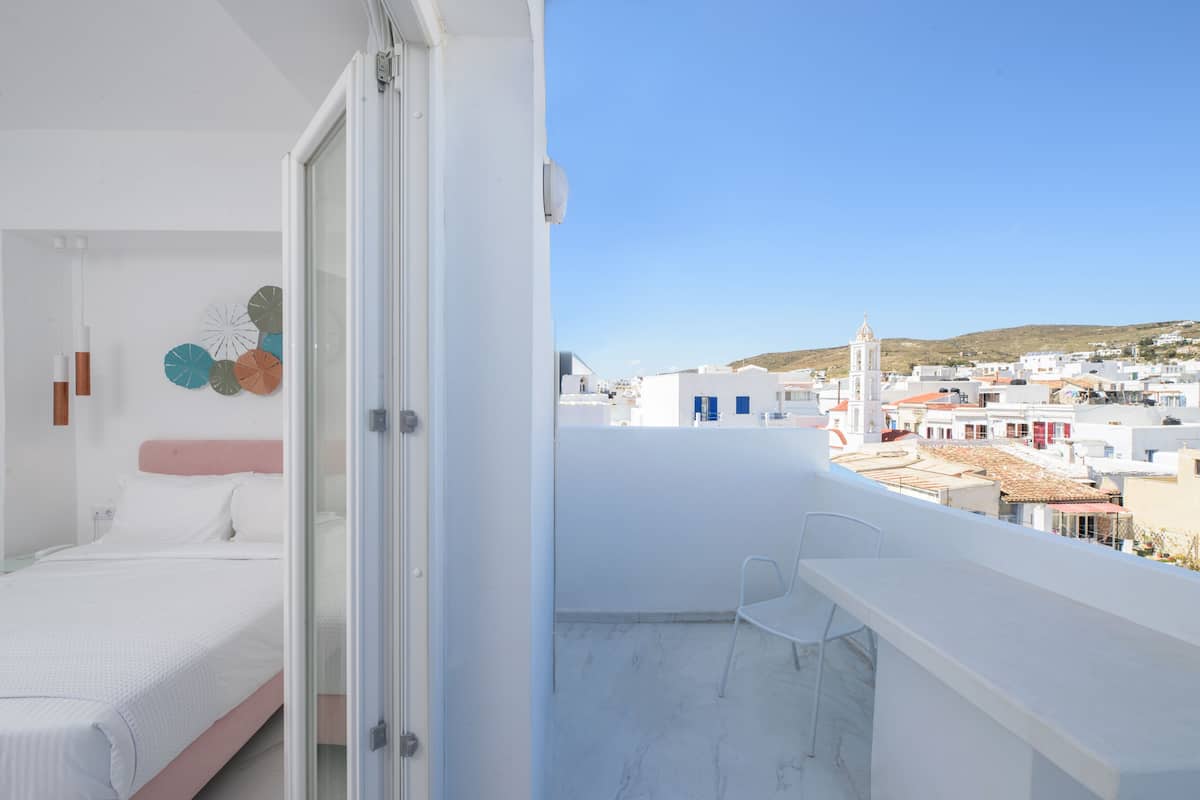 Ein Balkon mit freiem Blick auf eine Küstenstadt, ein Bett mit weißer Bettwäsche und ein Sessel.