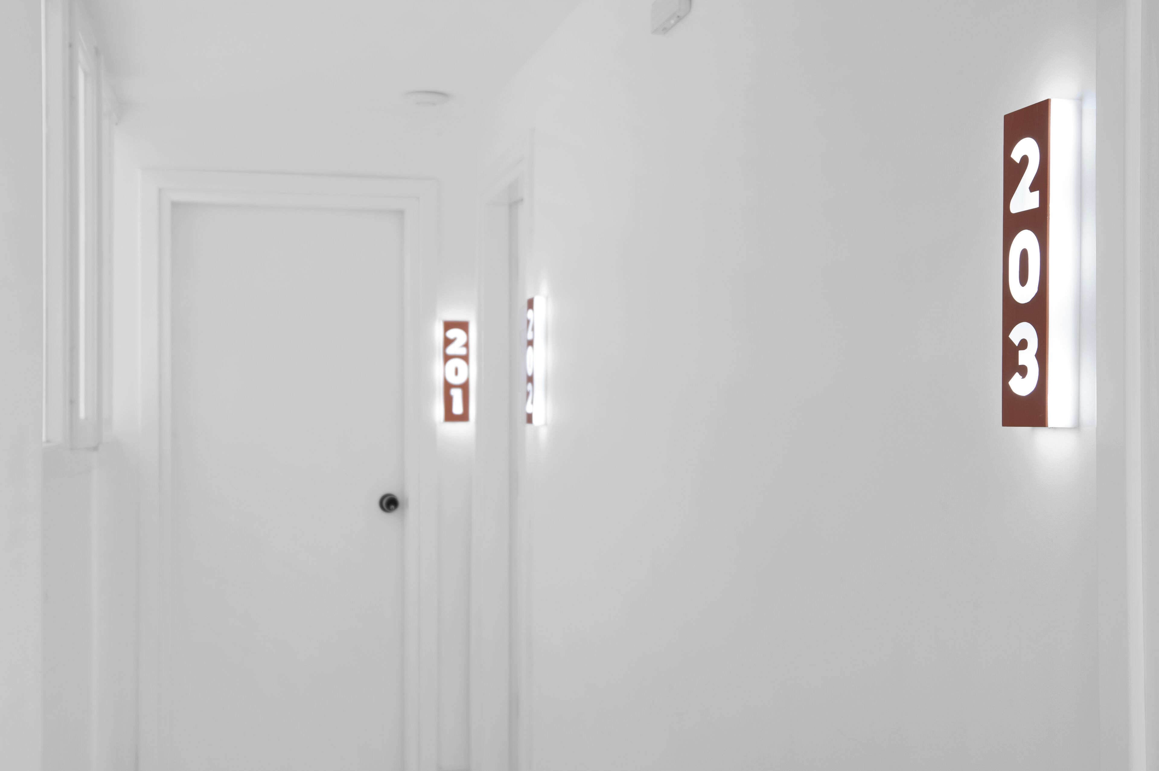 A hallway with a white door and illuminated room numbers '203' on the wall.