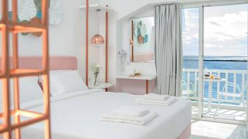 Un cuarto de hotel con una cama grande, una mesita de noche, un espejo y vista al mar.