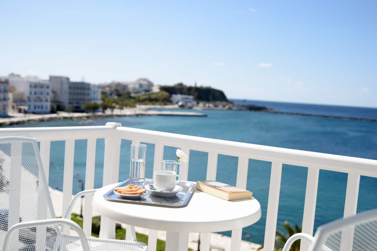 Ein Balkon mit einem weißen Tisch, gedeckt für das Frühstück, mit Blick auf die Küste, Gebäude und das Meer.