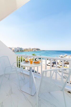 A balcony with white chairs and a table, overlooking a beach with a clear view of the sea and buildings in the distance. - Nama Boutique Hotel (Tinos)