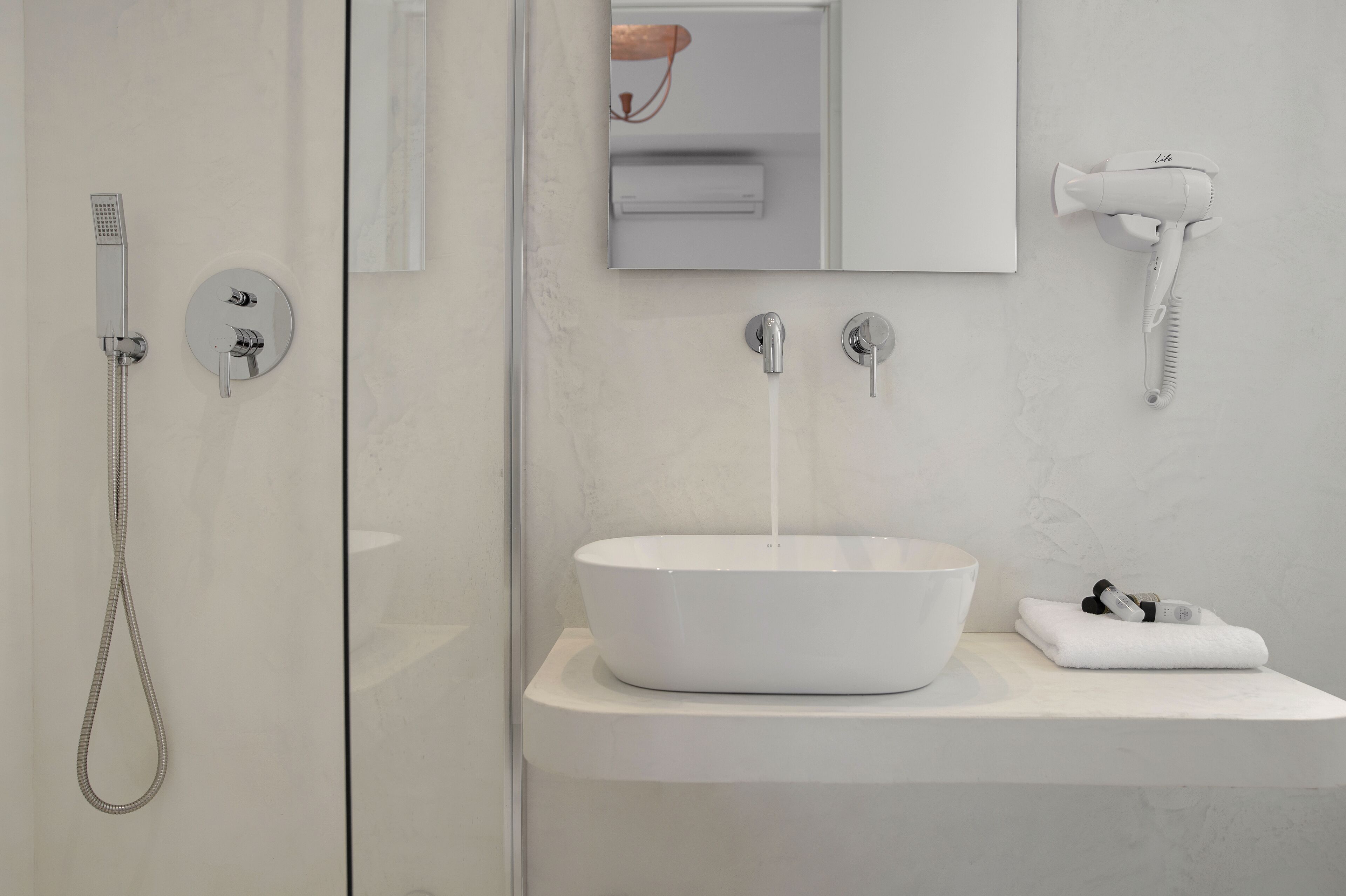 A modern bathroom with a white sink, a handheld showerhead, and a hairdryer mounted on the wall.