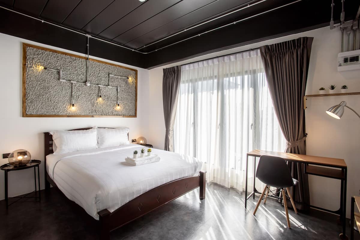 A modern bedroom with a large bed, a desk, and a large abstract painting on the wall.