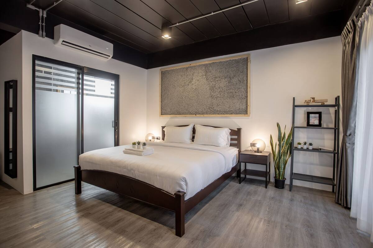 A modern bedroom with a large bed, bedside tables, a wall-mounted air conditioner, and a shelf with decorative items.