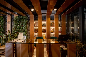 A reception area with a glass desk, a laptop, and a green chair. There is a wall with a plant and a brick wall with shelves. - My Loft Hotel (Chiang Mai)