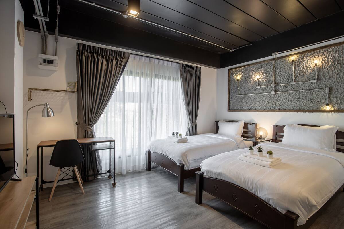 A modern hotel room with two beds, a desk, and a large window with curtains.