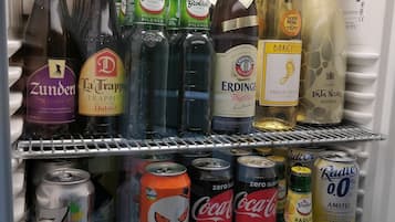 Un refrigerador lleno de diversas bebidas, incluyendo botellas de Zunder, La Trappist y Erdinger, así como latas de Fanta y Coca-Cola Zero Azúcar.