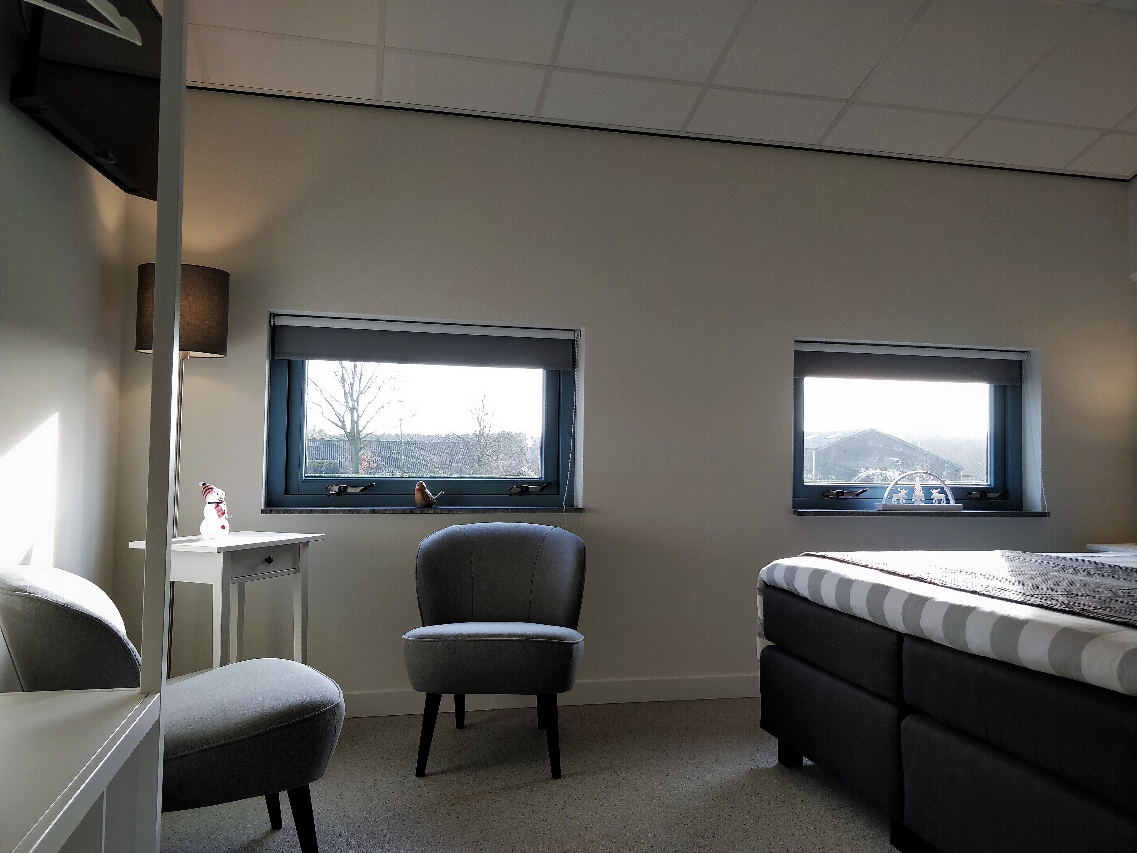 A bedroom with two windows, a chair, a bed, and a desk.