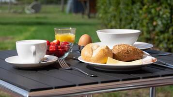 Een ontbijttafel met een kopje, kom, bord met brood, aardbeien en een glas jus d'orange.