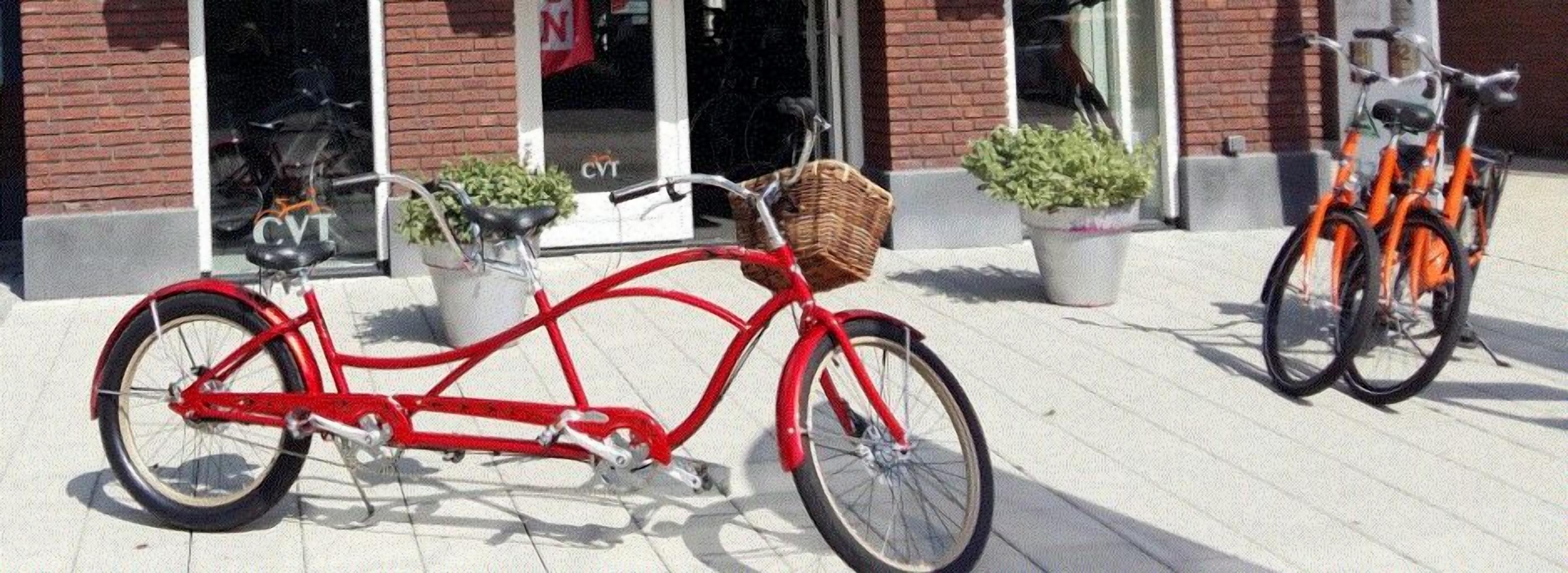 A red tandem bicycle parked on a tiled sidewalk in front of a building with a brick facade and a CVS store.