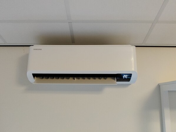 A white air conditioner mounted on a wall with a digital display showing 20 degrees. - Antonius Hoeve (Oudenbosch)