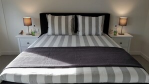 Een net opgemaakt bed met streepjesbeddengoed, twee nachtkastjes met lampen, en een klein decoratief object op elk tafeltje.