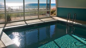 Une piscine intérieure avec des parois en verre transparent, offrant une vue sur l’océan, et une terrasse avec une rambarde.