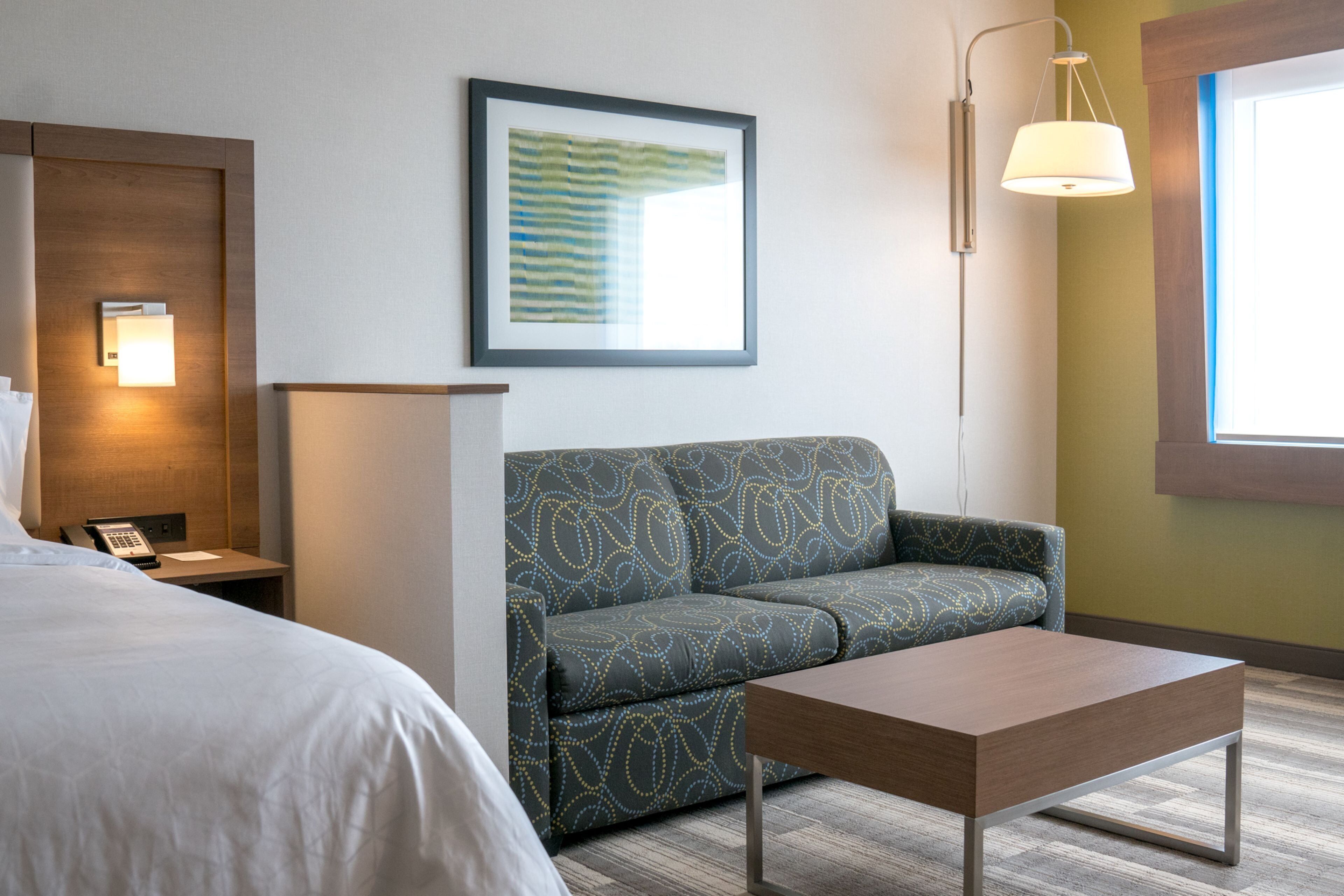 Une chambre d’hôtel avec un lit, un canapé, une petite table, un tableau encadré au mur et une lampe.
