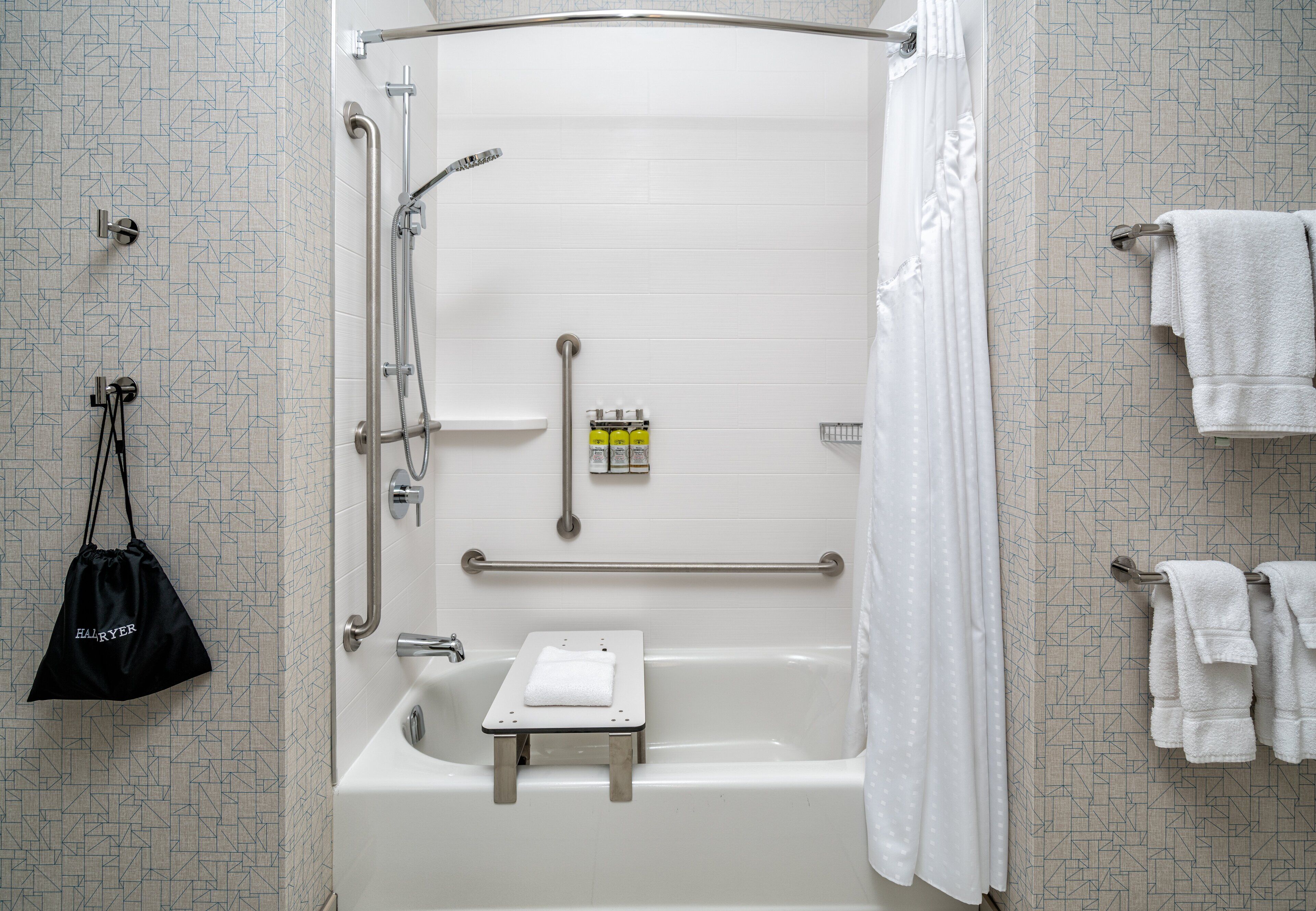 A modern bathroom with a walk-in shower, grab bars, a small step stool, and a towel rack.