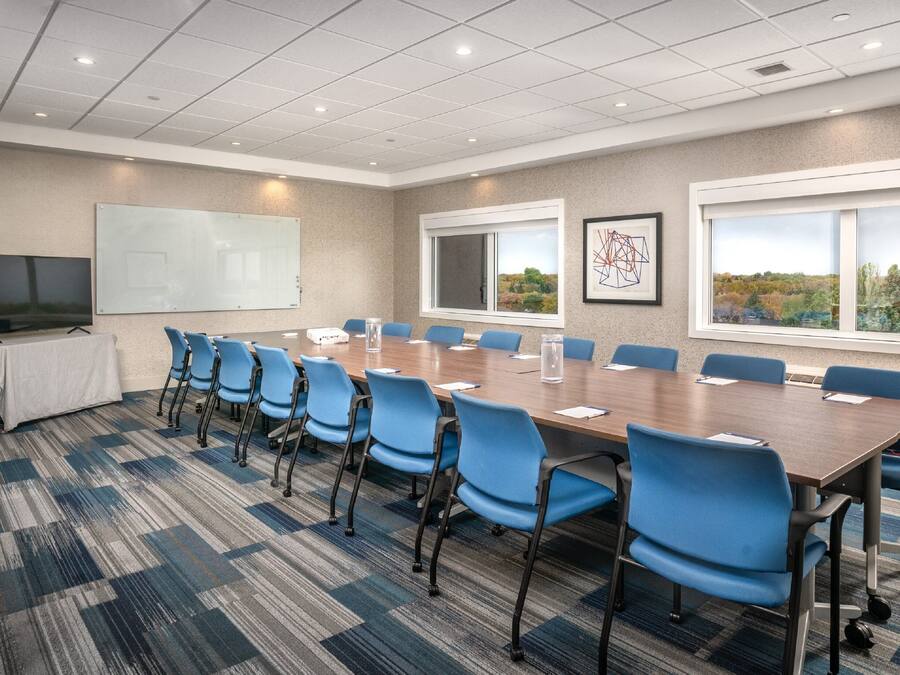 A conference room with a long table, blue chairs, a whiteboard, and a TV.