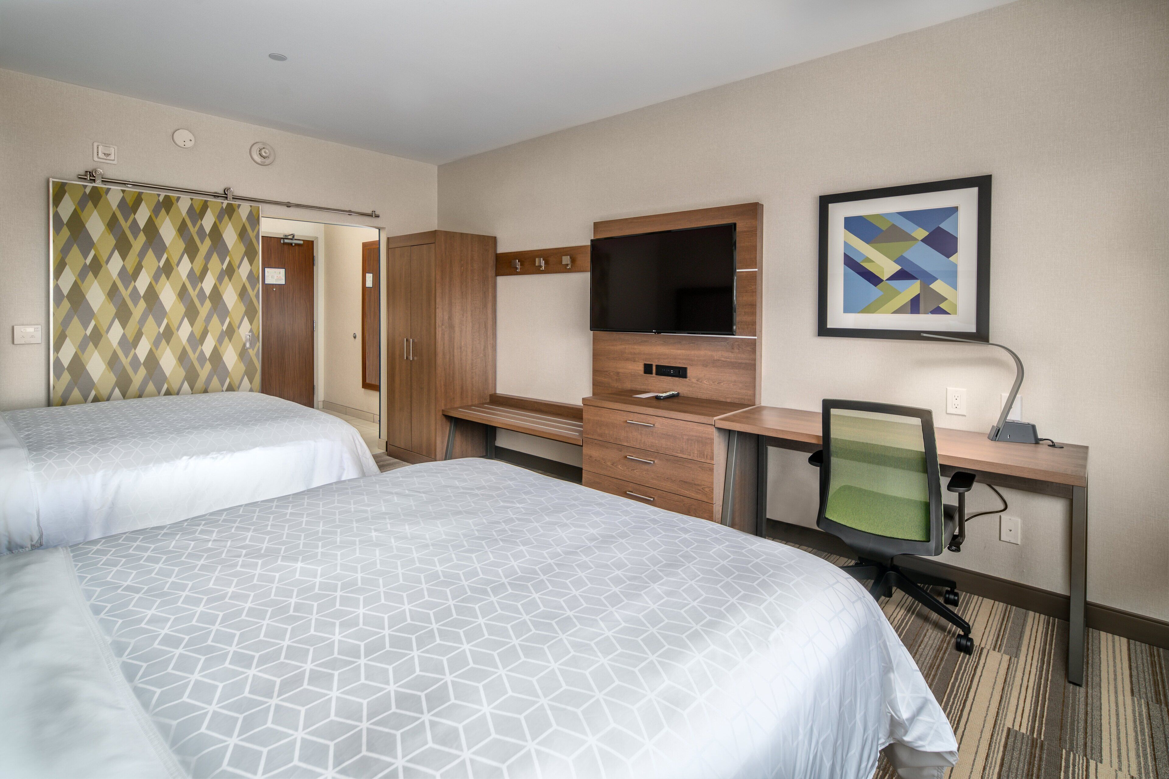 A hotel room with two beds, a desk with a computer, a TV, and a framed picture on the wall.