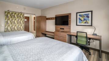 A hotel room with two beds, a desk with a computer, a TV, and a framed picture on the wall.