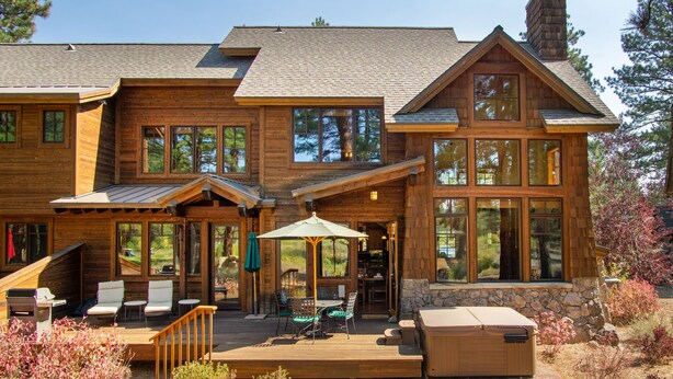 A wooden cabin with a deck, outdoor seating, and a hot tub.