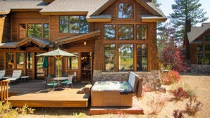 A large wooden house with a hot tub, outdoor seating, and a stone fireplace.
