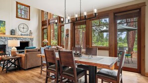 A spacious dining area with a wooden table and chairs, large windows offering a view of the outdoors, and a stone fireplace.