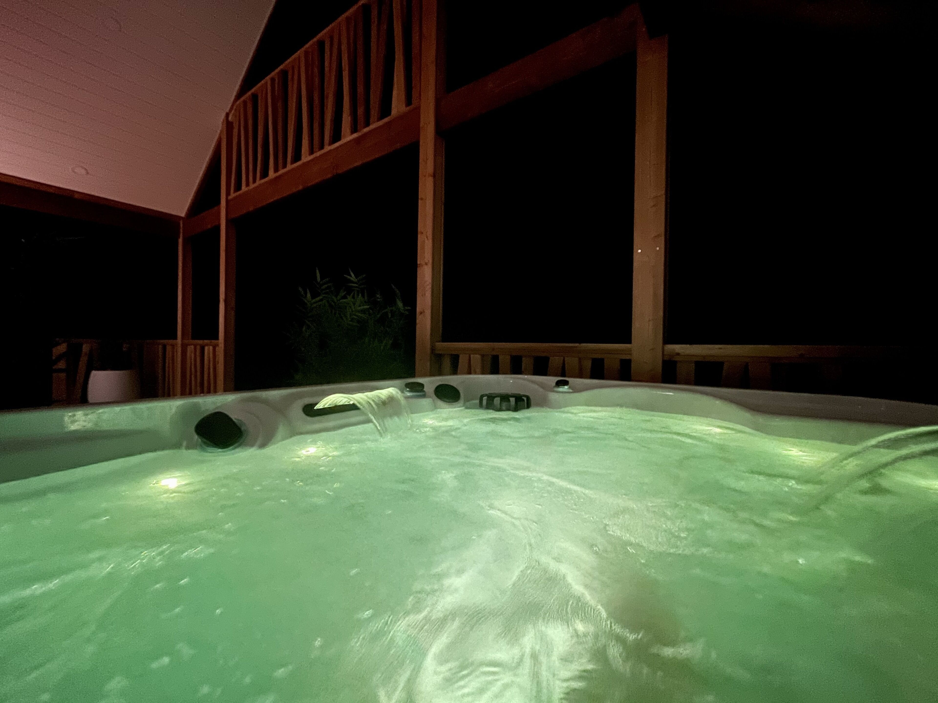 Un jacuzzi con cubierta de madera y barandillas, rodeado de oscuridad.