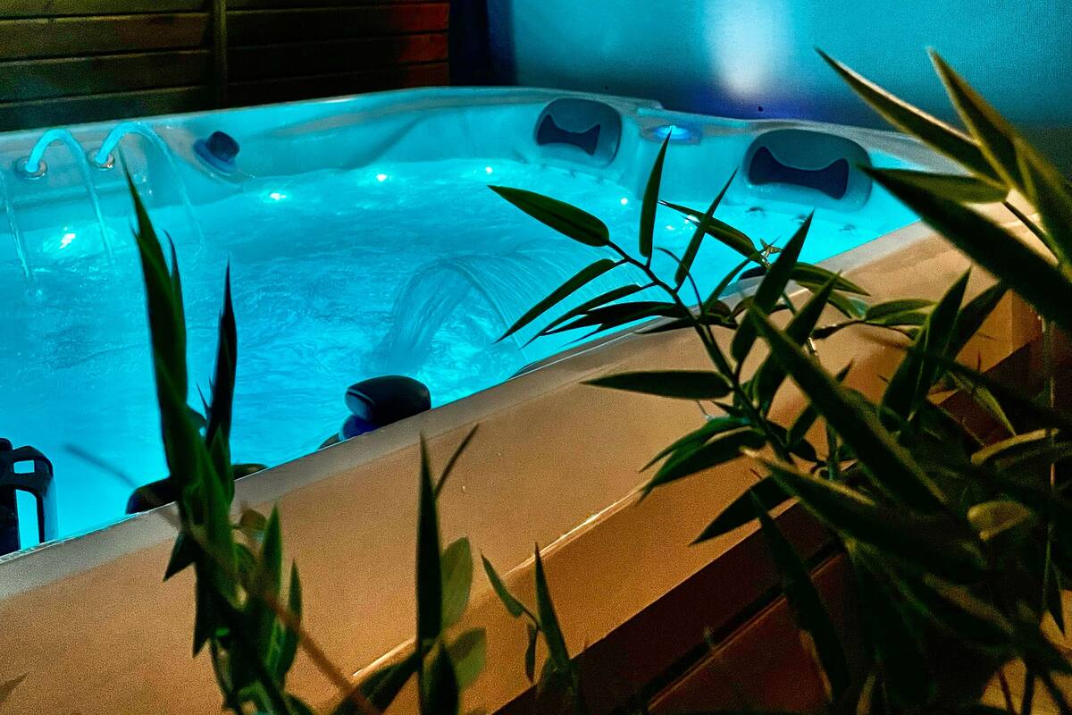 Uma banheira de hidromassagem com luz azul, rodeada por plantas e paredes de madeira.