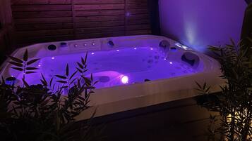 A hot tub with a wooden deck and bamboo plants.