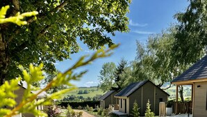 A row of wooden cabins with a gravel pathway leading to them, surrounded by greenery and trees. - Domaine les 2 Mondes (Aydat)