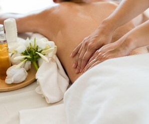 Une personne reçoit un massage avec une bouteille d’huile et des fleurs disposées sur un plateau.