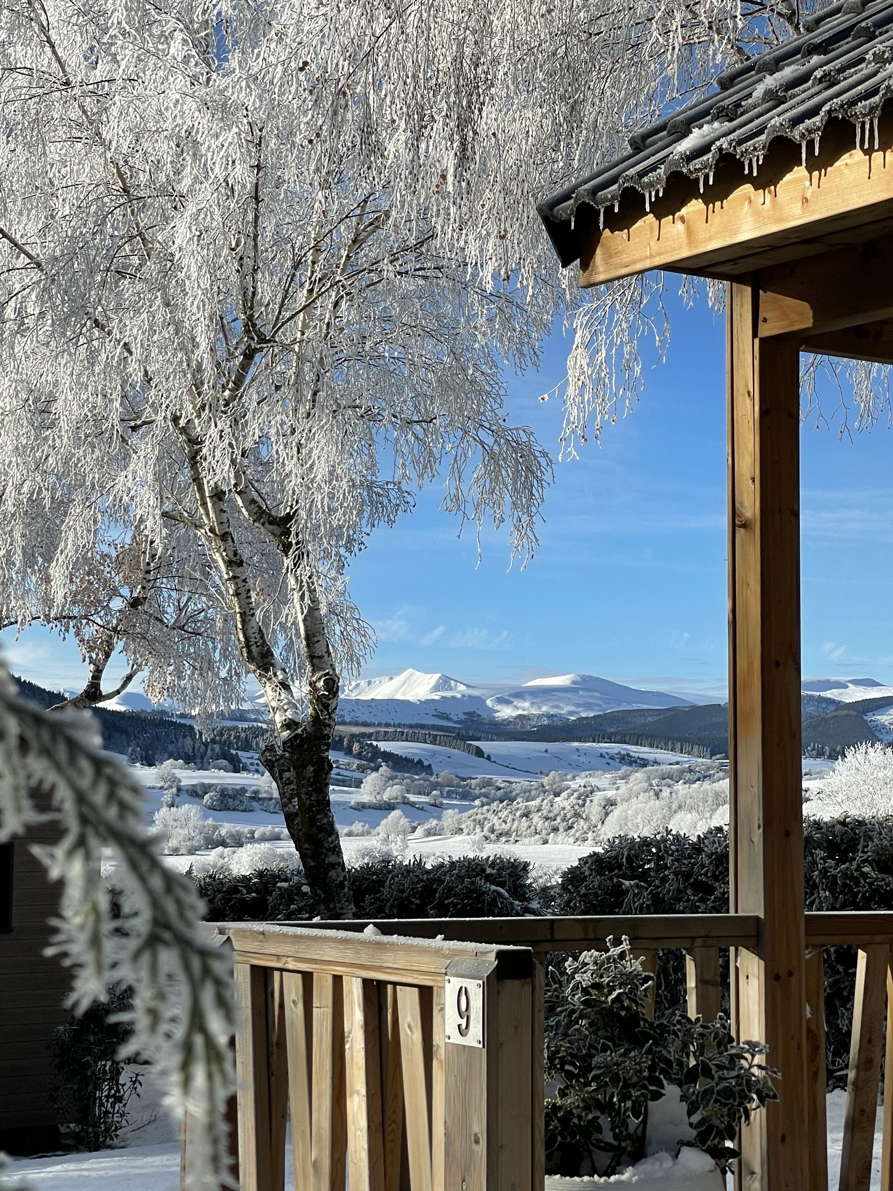 A wooden gazebo with a number '9' sign, overlooking a snowy landscape with trees and distant mountains.