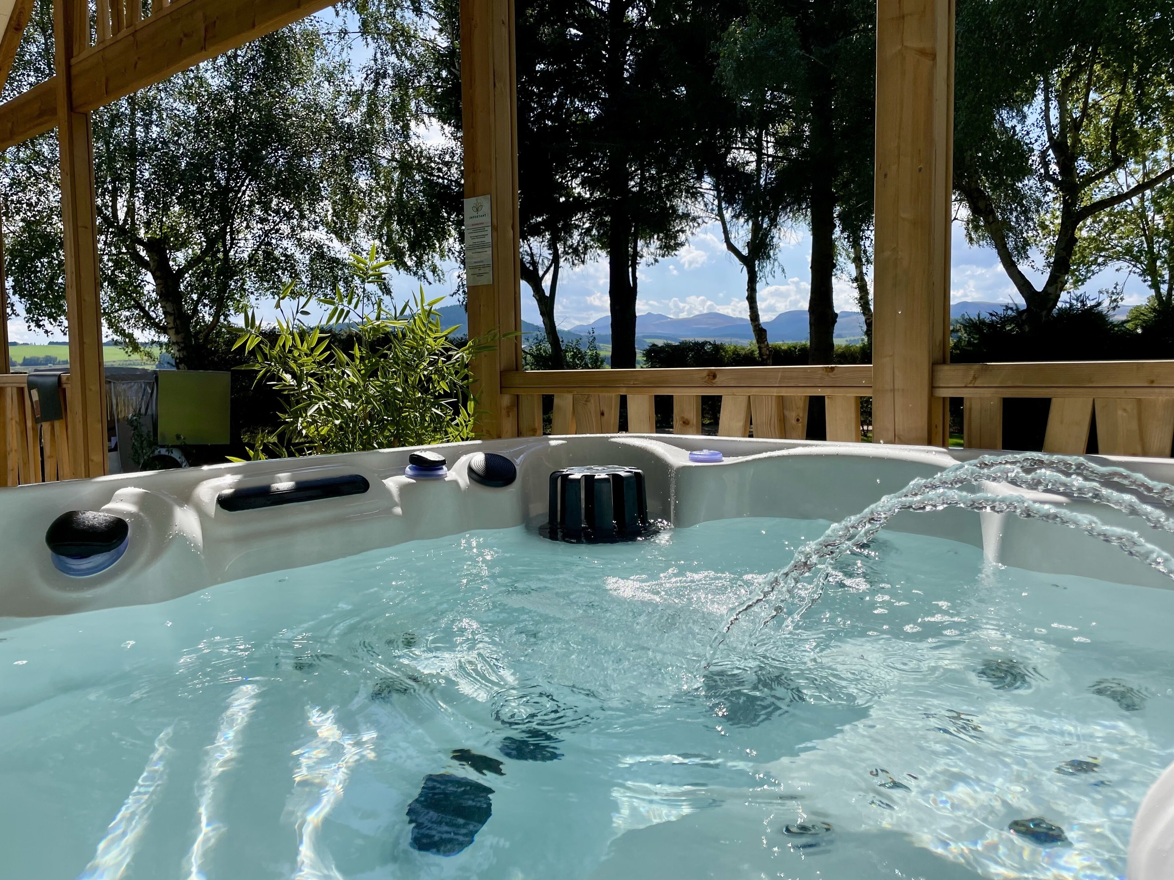 Un bain à remous avec de l’eau en mouvement, entouré d’une terrasse en bois et d’arbres, avec une vue sur les montagnes en arrière-plan.