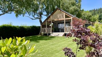 A wooden cabin with a balcony, surrounded by a well-maintained lawn and trees.