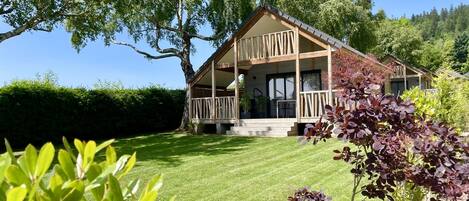 A wooden cabin with a balcony, surrounded by a well-maintained lawn and trees.