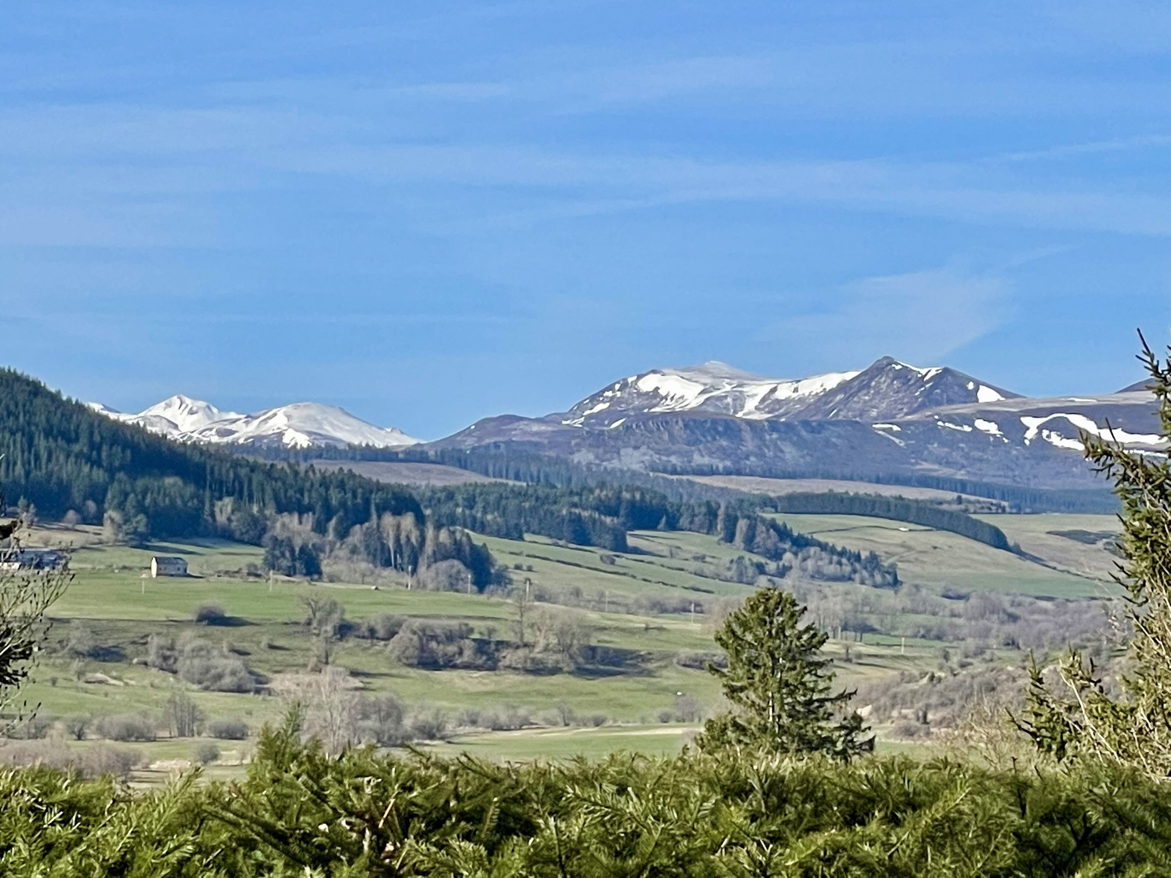 A mountainous landscape with snow-capped peaks, green valleys, and scattered trees.