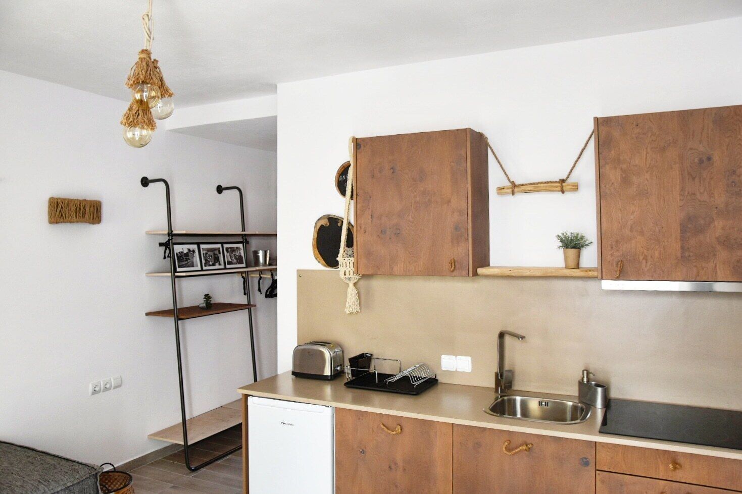 Una cocina compacta con armarios de madera, lavavajillas integrado, un lavabo y una lámpara colgante.