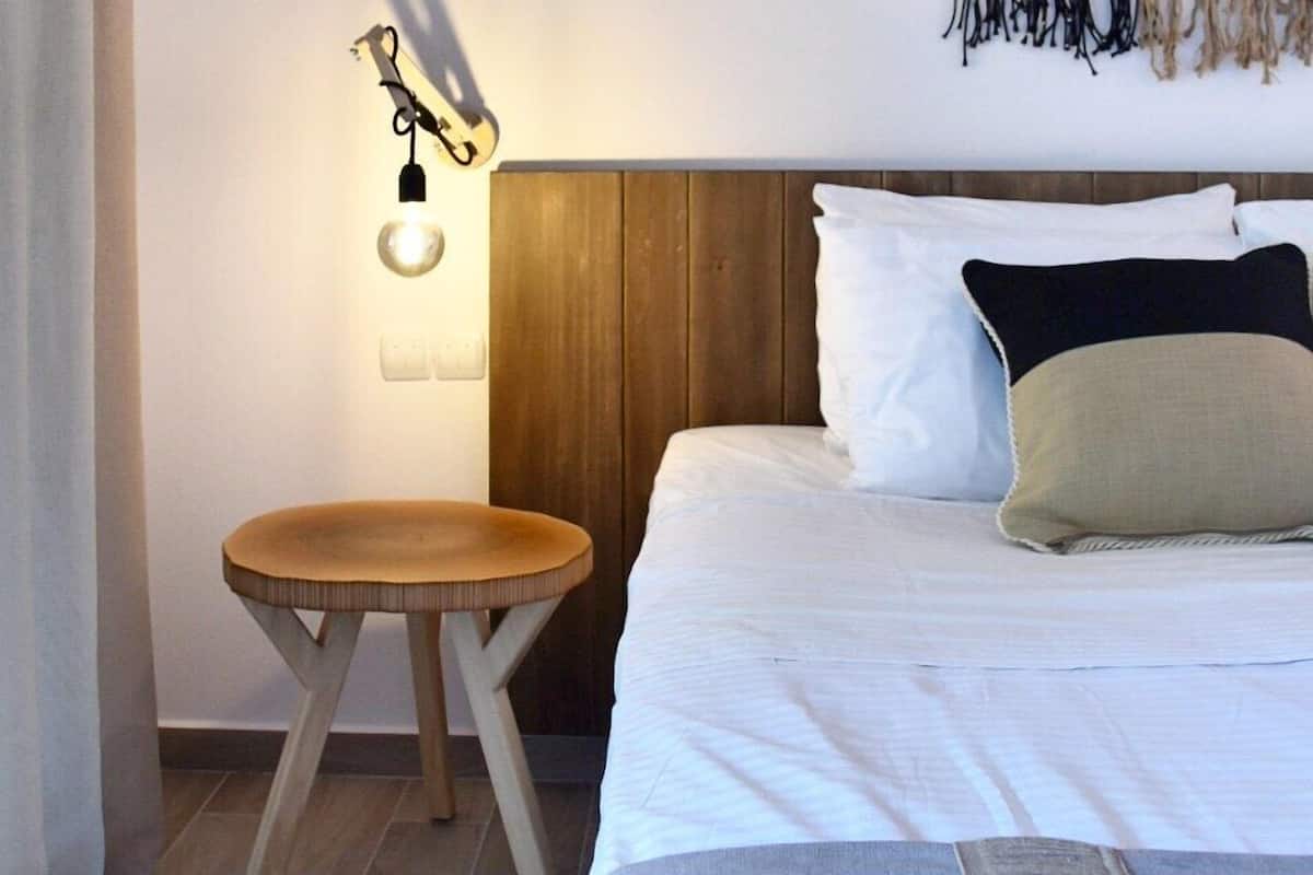 A bedroom with a wooden headboard, a round wooden stool, a wall-mounted light fixture, and a macrame wall hanging.