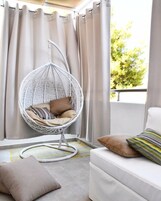 Una habitación con una silla colgante, un sofá y cortinas.