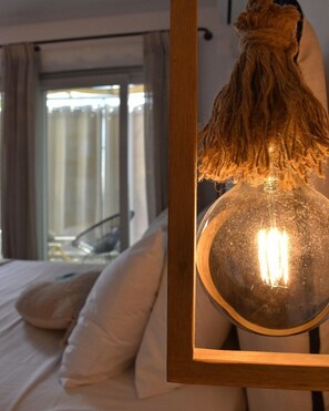 A bedroom with a bed, pillows, a window with curtains, and a hanging light fixture. - Angelos Boutique Suites (Alonissos)